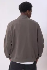 Campera bomber color marrón topo, con cierre frontal y bolsillos laterales con cierre. Tiene un bolsillo con cierre y etiqueta en la manga izquierda.