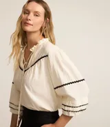 Blusa color crema de tricolina con detalles de ondas negras en cuello, mangas y frente. Tiene mangas 3/4 con volados y lazo en el cuello.