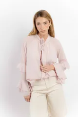 Blusa color rosa pálido de tejido fresco y liviano, con cuello alto con lazo y mangas largas con volados.