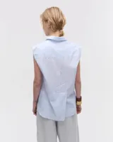 Camisa blanca sin mangas confeccionada en voile de algodón liviano. Tiene cuello camisero, cartera con botones de nácar, bolsillo plaqué en el delantero, costura en centro espalda y recorte en cintura trasera con tajo que se superpone. El ruedo es escalonado, más corto adelante.