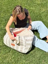 Bolso tipo tote extra grande de lona de algodón a rayas horizontales color beige y gris. Tiene doble asa de hombro, cierre superior y bolsillo exterior con etiqueta de cuero con logo.