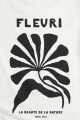 Remera de manga corta y cuello redondo, color blanco, con estampado frontal en negro que incluye la palabra "FLEURI", una ilustración abstracta de una hoja o flor y el texto "LA BEAUTÉ DE LA NATURE PARIS, 1978".