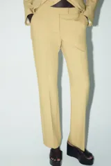 Pantalón color arena de tiro alto con bolsillos delanteros y corte acampanado. Cierre frontal con cremallera y gancho metálico.