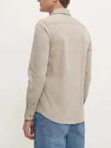 Camisa de vestir color beige claro, corte slim, de popelín de algodón elástico, con cierre frontal de botones y logo CK bordado en el pecho.