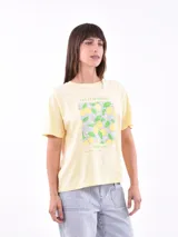 Remera color amarillo claro con estampado de limones, hojas y flores en tonos verdes y grises.