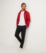 Chaqueta bomber roja de poliéster engomado, con cuello, puños y cintura acanalados a rayas blancas y azul marino. Tiene cierre frontal con cremallera y bolsillos laterales con cremallera.