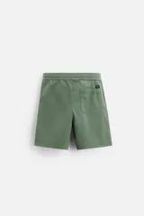 Bermuda color verde militar de corte relajado, confeccionada en tejido de algodón. Tiene cintura elástica ajustable con cordón interior, bolsillos frontales y bolsillo trasero de parche.