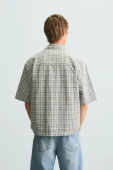 Camisa de hombre de corte boxy fit, confeccionada en tejido de algodón a cuadros en tonos beige, verde y azul. Tiene cuello solapa, manga corta y cierre frontal con botones.