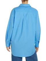Camisa celeste de popelín de algodón orgánico, corte oversize con hombros caídos, cuello inglés, bolsillo de parche en el pecho y logo bordado en la manga.