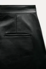 Pantalón de cuero negro de tiro medio, con pinzas delanteras, bolsillos laterales ocultos y corte holgado.