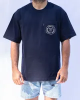 Remera azul marino de algodón con bolsillo en el pecho y estampado circular con la inscripción "Denali Durable Goods. Nacimos para algo".