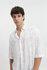 Camisa oversize blanca con estampado de hojas en color gris. Tiene cuello clásico, manga corta y cierre con botones.
