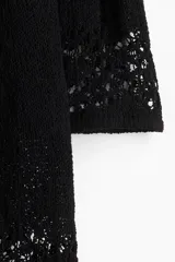 Vestido mini negro de manga larga en tejido de punto suave con escote redondo y falda con leve vuelo. Presenta secciones caladas en mangas, delantero y espalda, y secciones en punto pointelle en puños y bajo.