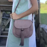 Bandolera marrón con solapa curva y cierre magnético. Presenta costuras decorativas en la solapa, bolsillo tipo guantera frontal y tassel decorativo. Incluye correa larga regulable y bolsillos internos.