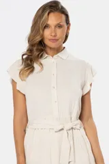 Vestido corto color beige de lino, con cuello camisero, mangas cortas con volados, cierre frontal con botones y lazo para ajustar en la cintura.