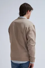 Sudadera de tejido liso color beige, con cuello redondo y puños y ruedo acanalados. Se lleva superpuesta a una camisa de cuadros celestes y blancos.