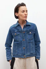 Chaqueta de jean azul medio, de corte clásico, con cuello camisero, bolsillos con solapa en el pecho y cierre frontal con botones metálicos color cobre.