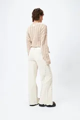 Pantalón de denim blanco con calce wide leg y ruedo desflecado. Presenta tachas metálicas a lo largo de los laterales.
