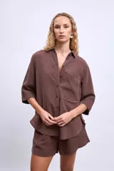 Camisa blanca de manga tres cuartos, con cuello camisero y corte holgado. Presenta un bolsillo de parche en el pecho izquierdo.