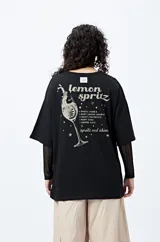 Remera blanca de corte holgado con mangas cortas y cuello redondo. Estampado pequeño en el frente con la frase "Spritz and Shine" en verde.
