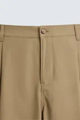 Pantalón color beige de corte ancho, con pliegues frontales dobles, bolsillos laterales y traseros de vivo. Largo cropped y cierre frontal con cremallera y botón.