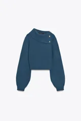 Jersey de punto azul con cuello solapa y botones dorados en el hombro. Tiene manga larga abullonada.