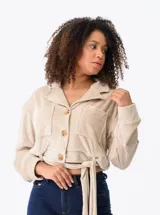Campera color beige de textura suave, con cuello camisero, cierre frontal con botones, dos bolsillos de parche en el pecho, mangas largas con puños abotonados y lazo en la cintura.