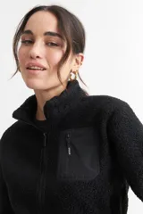Campera negra de corderito con cierre frontal y cuello alto. Tiene un bolsillo con cierre en el pecho y bolsillos laterales.