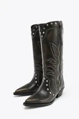 Bota de caña alta color marrón oscuro con bordados en contraste y tachas plateadas. Cierre con cremallera frontal y tacón bloque bajo.