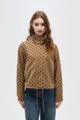 Campera color camel con estampado de lunares negros, cuello alto y cierre frontal. Tiene mangas largas y cordón ajustable en el dobladillo.
