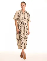 Vestido maxi de crepe color beige con estampado floral en tonos marrones y negros. Presenta cuello a la base, escote en V, abertura central con botones y cintura con lazo de ajuste y hebilla.
