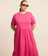 Vestido midi fucsia de algodón, con cuello redondo, mangas cortas, corte a la cintura y falda amplia con volantes.