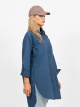 Vestido camisero corto, color azul, con cuello solapa, manga larga y bolsillo delantero de plastrón. Presenta un bajo asimétrico.