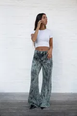 Jean de mujer de corte recto y tiro alto, con efecto acid wash en tonos gris y verde claro. Presenta costuras frontales y traseras que simulan pliegues, y etiqueta de marca blanca en la parte trasera de la cintura.