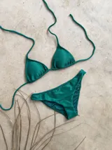 Conjunto de bikini verde esmeralda con textura acanalada. El corpiño es de triángulos movibles con tiras finas para atar al cuello y a la espalda, y tiene almohadillas desmontables. La bombacha es vedetina ancha con laterales fijos.