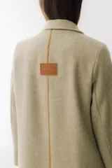 Tapado largo color beige con diseño de espiga, apliques de cuero marrón en bolsillos y mangas, tajos laterales y cierre con botón.