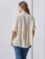 Blusa color crema de crepe con cuello a la base con solapa, escote en V con abertura central y botones. Delantera con detalles plisados y apliques en crochet. Manga corta con terminación fruncida y ruedo en broderie.