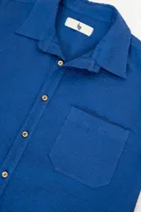 Camisa azul de manga corta confeccionada en algodón ligero con textura waffle. Presenta un corte cuadrado, bolsillo en el pecho y botones de coco con el logo de Polonio.
