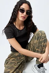 Remera negra de punto acanalado con cuello redondo y mangas cortas. Presenta apliques de strass en el escote y las mangas.