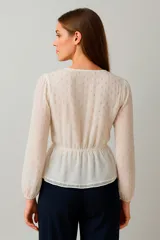 Blusa color marfil con escote en V, mangas largas abullonadas y detalle de lazo en el centro del busto.