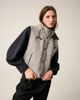 Chaleco matelaseado color gris con cuello alto, cierre frontal y capucha ajustable, perfecto para superponer.