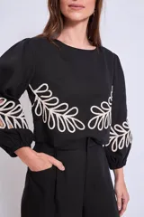 Blusa negra con cuello redondo y mangas largas abullonadas, con apliques bordados de hojas en color crudo en el frente y en las mangas.