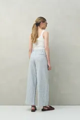 Pantalón de lino a rayas verticales azules y blancas, de corte amplio y relajado, con bolsillos laterales y cierre frontal con botón.