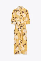 Vestido midi camisero color amarillo con estampado de flores blancas y hojas marrones. Tiene cuello solapa, mangas 3/4 con puños, cinturón de lazo ajustable y cierre frontal con botones.