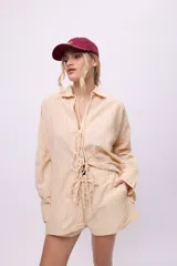 Camisa blanca de lino y algodón, con cuello clásico, cierre frontal con lazos y mangas largas abullonadas con puños ajustables con lazos.