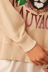 Buzo color beige de algodón con cuello redondo y mangas largas. Estampado frontal con un tigre, flores y la frase 'Liberté Sauvage'.