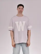 Remera color lila con estampado de la letra W en el centro y dos rayas blancas en las mangas cortas.