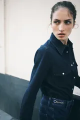 Jeans de tiro alto, pierna ancha y corte recto, confeccionado en denim de algodón rígido de color azul medio. Presenta un detalle de herrajes metálicos en la cintura.