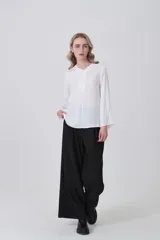 Blusa blanca de poliéster, entallada, con escote en V y botones frontales. Presenta mangas largas con puños anchos.