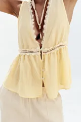 Blusa amarilla sin mangas con escote en pico y detalle de puntillas blancas. Cierre frontal con botones.